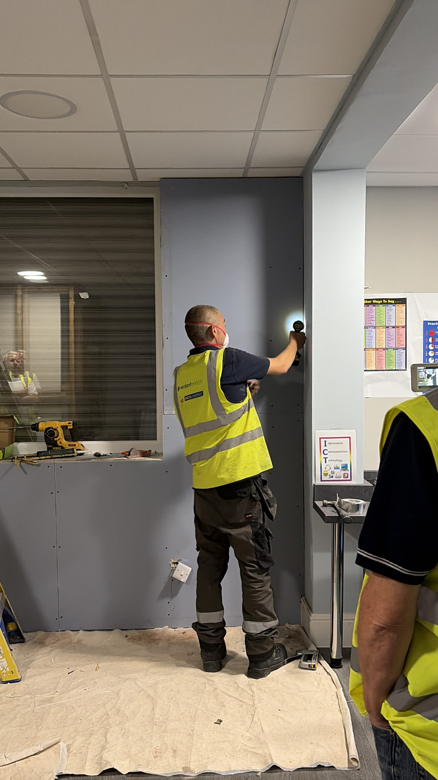 A man using a drill to drill plasterboard on to a wall. 