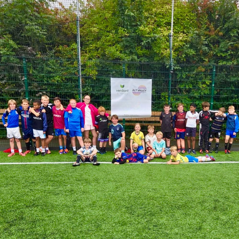 A group of around 20 young children dressed in football kits stood on a pitch.